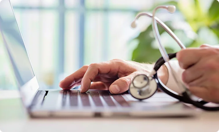 Telemedicine provider typing for HIPAA compliance on a laptop holding stethoscope